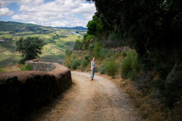 A woman walking along a path that leads to a vineyard, surrounded by the vibrant green landscape of the Douro Valley.