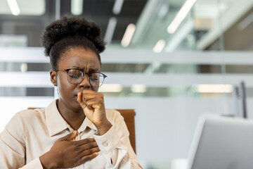 African American businesswoman experiencing discomfort and coughing in office. Depicts stress,...