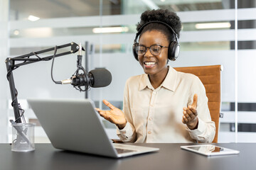 Confident African American businesswoman recording podcast with headphones and microphone using...