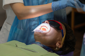 Close-up view of female patient in protective eyeglasses with installed cheek retractor lying on...
