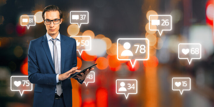 Attractive happy young european businessman using tablet with creative social media icons on blurry bokeh background. Communication and networking concept.