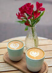 Two flatwhites on a table with red flowers 