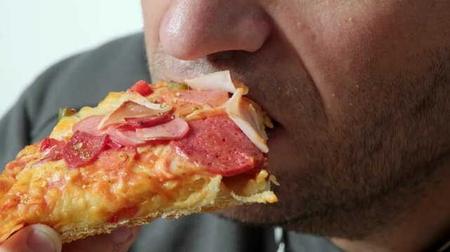 A close-up video showing a man taking a bite of a pizza slice, highlighting the texture of the pizza and the man's mouth as he eats