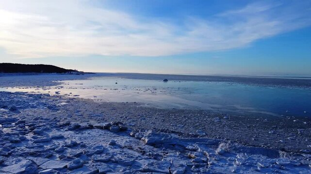 Une baie d'eau froide glac&eacute;e avec le reflet du soleil &agrave; contre-jour sous un ciel bleu nuageux avec une langue de terre en arri&egrave;re-plan. ( Baie-des-Sables, Fleuve Saint-Laurent, Qu&eacute;bec, Canada. )