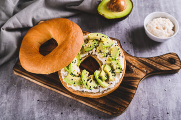 Bagel burger with ricotta, avocado and sesame seeds on a board on a table