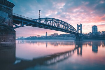 Fototapeta premium A majestic bridge gracefully arches over a tranquil river, reflecting the city's skyline bathed in the soft glow of a picturesque sunrise.