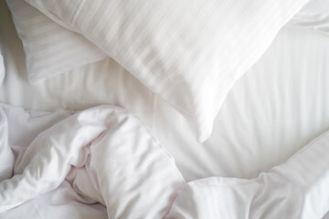 Unmade bed with crumpled blanket and hypoallergenic pillow on clean bedsheets