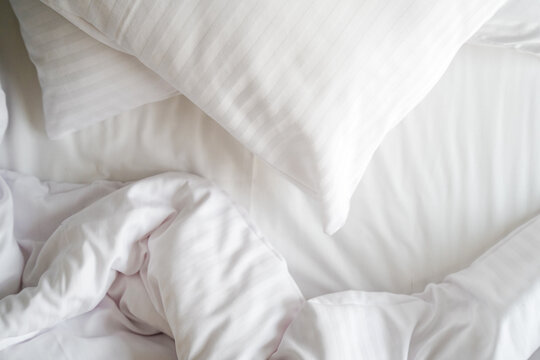 Unmade bed with crumpled blanket and hypoallergenic pillow on clean bedsheets