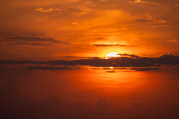 Obraz premium A view of the setting sun in the sky, partially hidden behind layers of clouds. Intense shades of orange, red and gold. An idea for a background or wallpaper.