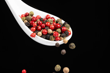 Different types of peppercorns pouring. Red, green, white and black pepper.