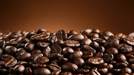 Dark coffee beans tumble onto a pile, filling the frame against a warm brown backdrop.