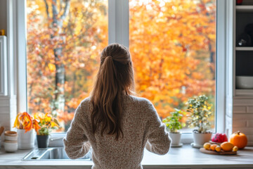 Backview of woman looking out kitchen window at vibrant autumn foliage