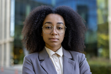 Confident African American business woman with curly hair and glasses standing outdoors, showcasing professionalism and leadership qualities. She reflecting strength and determination in a corporate