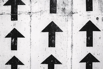 Monochrome pattern of upward black arrows painted on a white concrete wall creating a bold graphic urban design