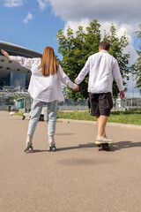 Fototapeta premium Young couple rollerblading and skateboarding in park. Happy and joyful girl and man doing sports together on warm summer day. Vertical photo. High quality photo