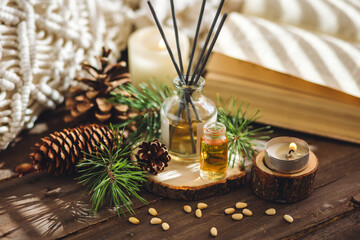Christmas home aromatherapy. Aroma diffuser with pine extract, organic essential oil, cedar and spruce cone, candles on wooden table. Cozy atmosphere, holiday spirit. Winter inspiration and mood.