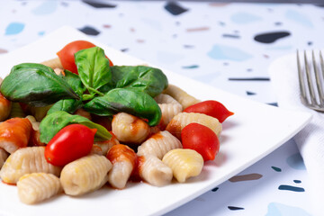 A plate of gnocchi with sauce, tomato and basil leaves.