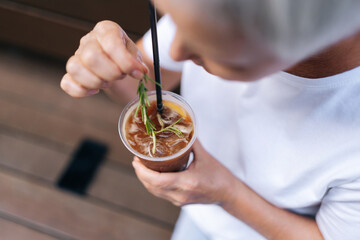 Closeup top view of unrecognizable woman holding cup of iced coffee with straw in urban setting on summer day. Cup of cold bubble tea with straw in female hand. Concept of drink, lifestyle, city life