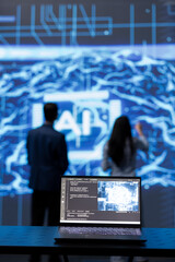 Focus on complex AI brain models being analyzed on laptop by developers in blurry background. Close...