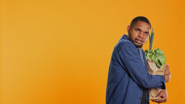 Vegan person acting overprotective of his eco friendly groceries bag, protecting his freshly harvested goods in studio. Serious man taking care of his bio organic belongings. Camera B.
