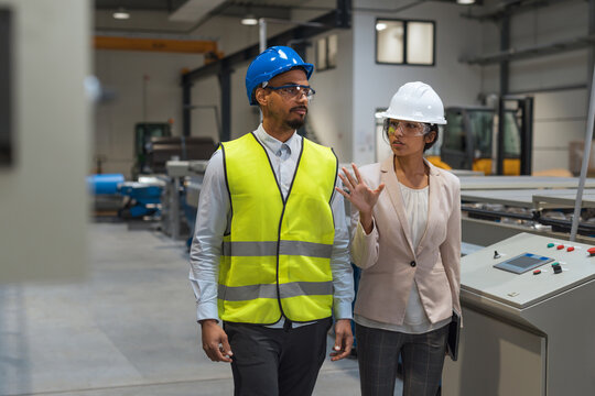 Indian female factory manager introducing the production line to a recruit, an African American worker, and congratulating him on a new job, front view. - Powered by Adobe