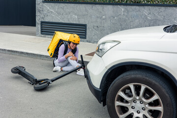 Latin girl courier with yellow backpack and helmet in pain on the ground after being hit by a car