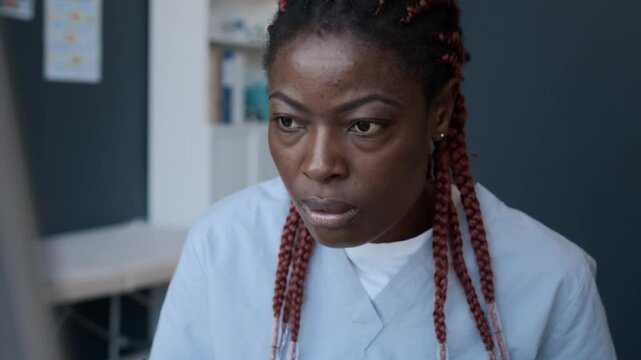 Close up view of focused African American female doctor making notes and managing patients appointments on computer at workplace