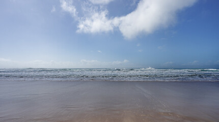 A surf beach with shoreline, wet sand and rough breaking waves and blue sky with clouds on a winter day on the Sunshine Coast Queensland
