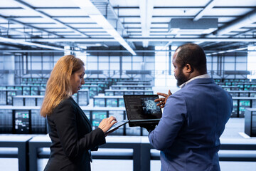 Teamworking colleagues using AI software on laptop, programming in AI data center. IT staff members...