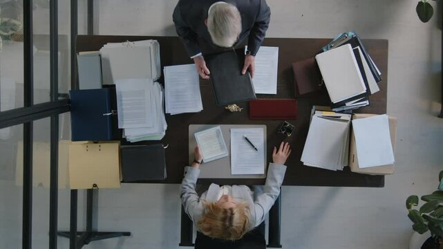 Top down view of two lawyers working with papers in office, senior man putting folder on desk, woman scrolling document on digital tablet
