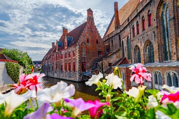 Naklejka premium On a lovely summer day in Bruges, Belgium, a charming canal is lined with vibrant flowers and historic buildings, making it an ideal spot for romantic getaways and relaxing vacations.
