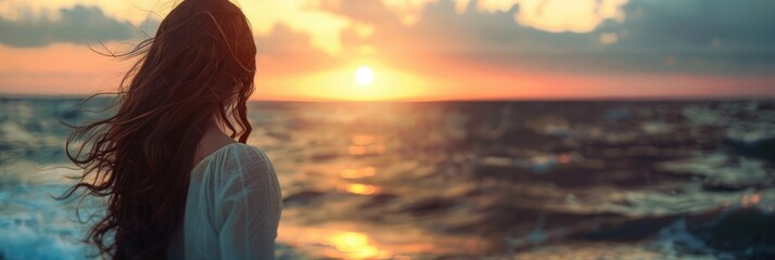 Fototapeta premium Girl with long dark hair appreciating a sunset by the ocean