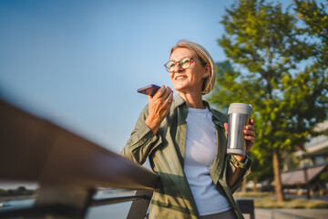 mature woman hold thermos and record voice mail in front the river