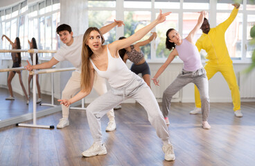 Obraz premium Young woman conducts lesson for young people, teaches guys and girls to move aesthetically to beat of music, control their bodies and perform modern urban dances