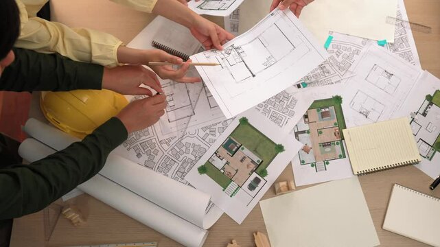 Architect and safety engineer discussion about building construction use blueprint on table with architectural document, measurement tool and wooden block scatter around at modern office. Delineation.