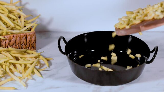 Sliced beans are poured from a wooden board into a cooking pot, whole runner beans in the background