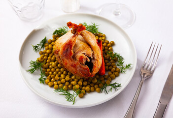 Popular dish of Spanish cuisine is baked quail served with carrots, canned peas and decorated with...