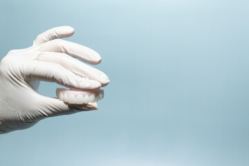 Dentist Holding Denture Model with Gloved Hand on Blue Background