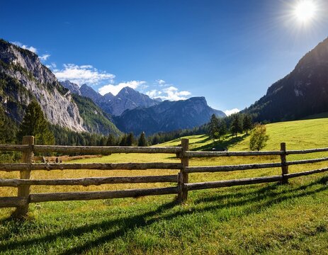 Wooden fence in field with mountains, blue skies and white clouds.