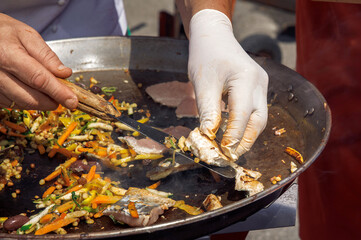Chef grilling fresh fish, cooking at outdoor food festival, hands in gloves, street food, culinary...