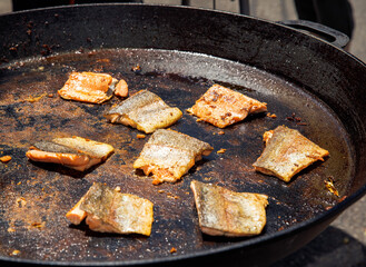 Grilled salmon fillets cooking in large pan on outdoor stove with golden crust, summer barbecue concept