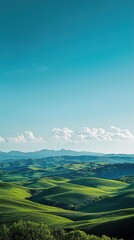 Obraz premium Rolling green hills stretch across the landscape under a clear blue sky. The vibrant green of the hills contrasts with the deep blue of the sky, creating a picturesque scene. In the distance, a range 