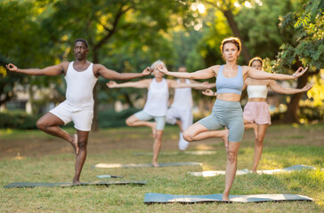 Group of multinational people practitioner performing Garudasana in sunny garden