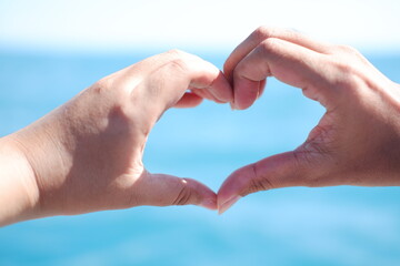 Hands forming a heart shape with the sea in the background.