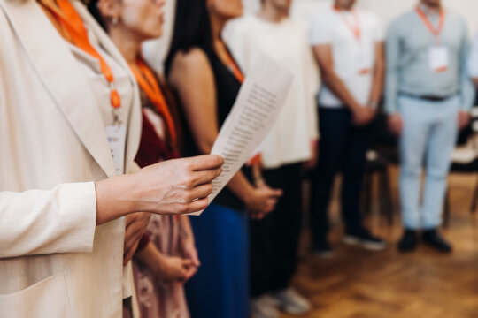 Choir rehearsal, vocal class singing in the auditorium hall, group of students on stage holding white sheets and singing, orchestra vocals class in music school with a teacher, adults sing in chorus