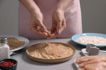 Making schnitzel. Woman coating slice of meat with bread crumbs at grey table, closeup