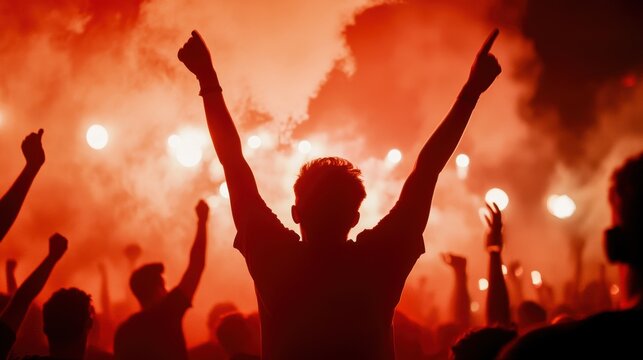 Dynamic crowd raising hands in celebration, illuminated by vibrant red flares, creating an electrifying atmosphere of excitement.