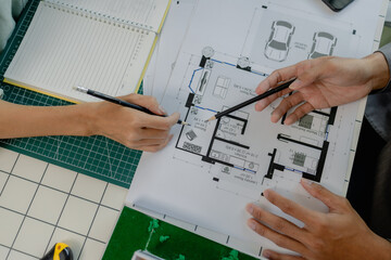 engineers are sitting discussing a construction plan that needs to be revised to make the structure stronger, an architect and assistant are brainstorming and examining the blueprints
