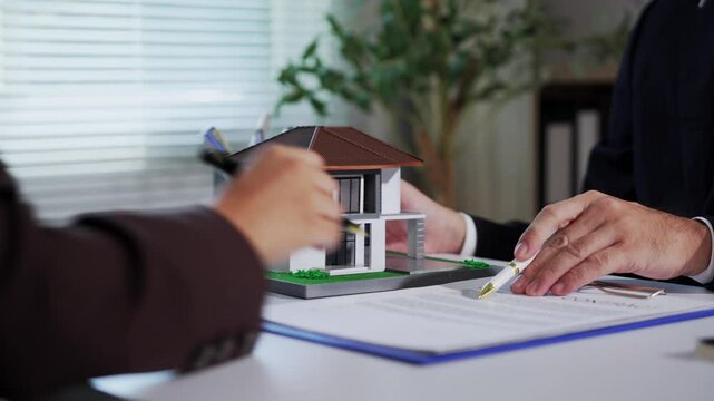Businessman showcasing a small house model to a client while discussing contract details during a consultation in an office environment