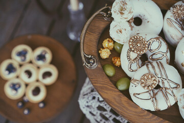 Some well decorated donuts with frosting are displayed on a wooden plate. Some egg tarts in another...